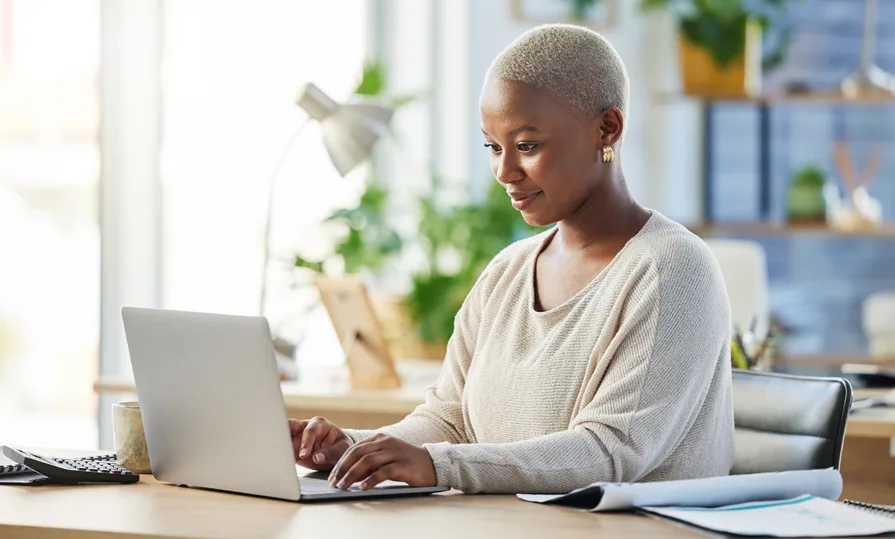 Woman sitting at a desk researching home warranty options on her laptop, symbolizing the decision-making process for choosing the right coverage.