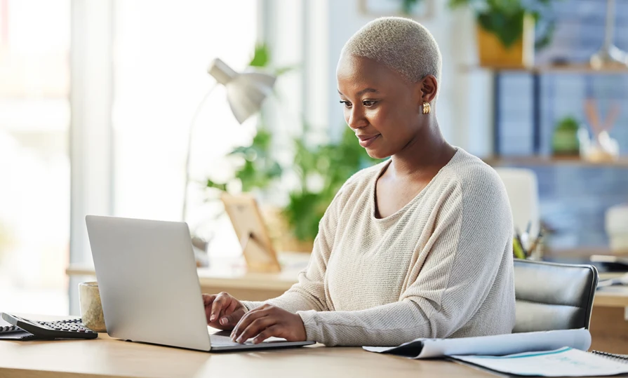 Woman sitting at a desk researching home warranty options on her laptop, symbolizing the decision-making process for choosing the right coverage.