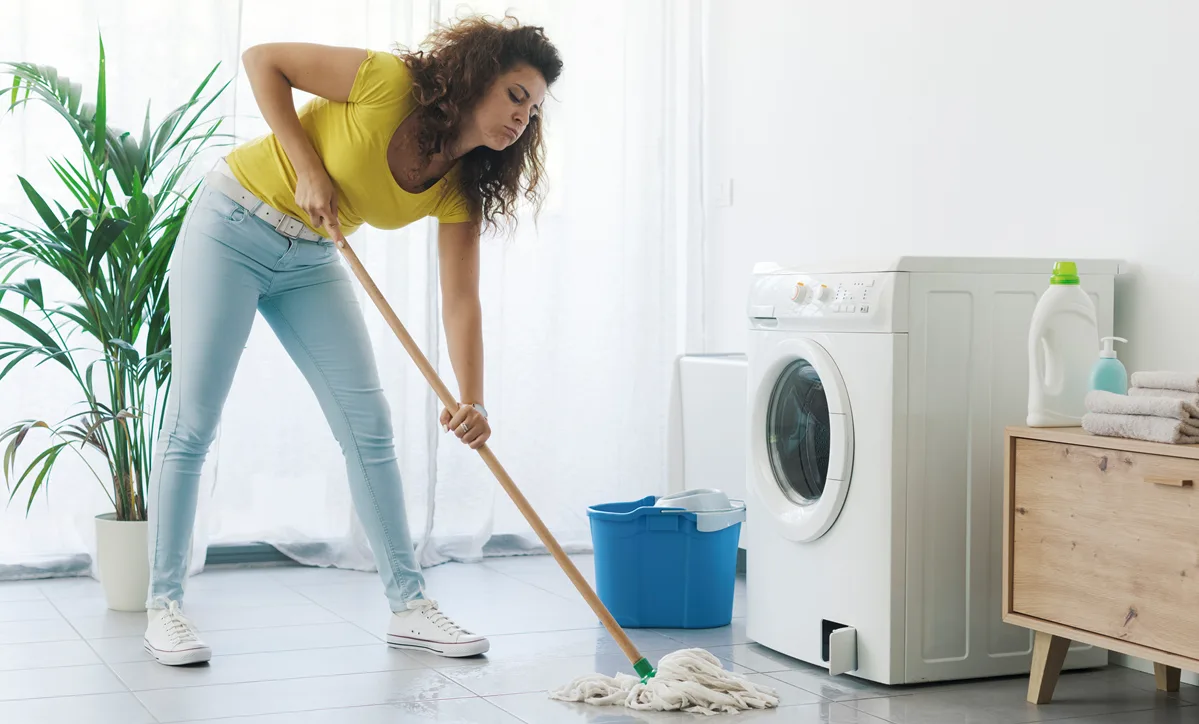 Homeowner mopping up water from a leaking washing machine and understanding why she needs a home warranty to fix broken appliances.