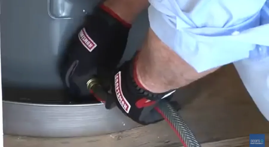 A homeowner connects a hose to the water heater drain valve to drain the tank.
